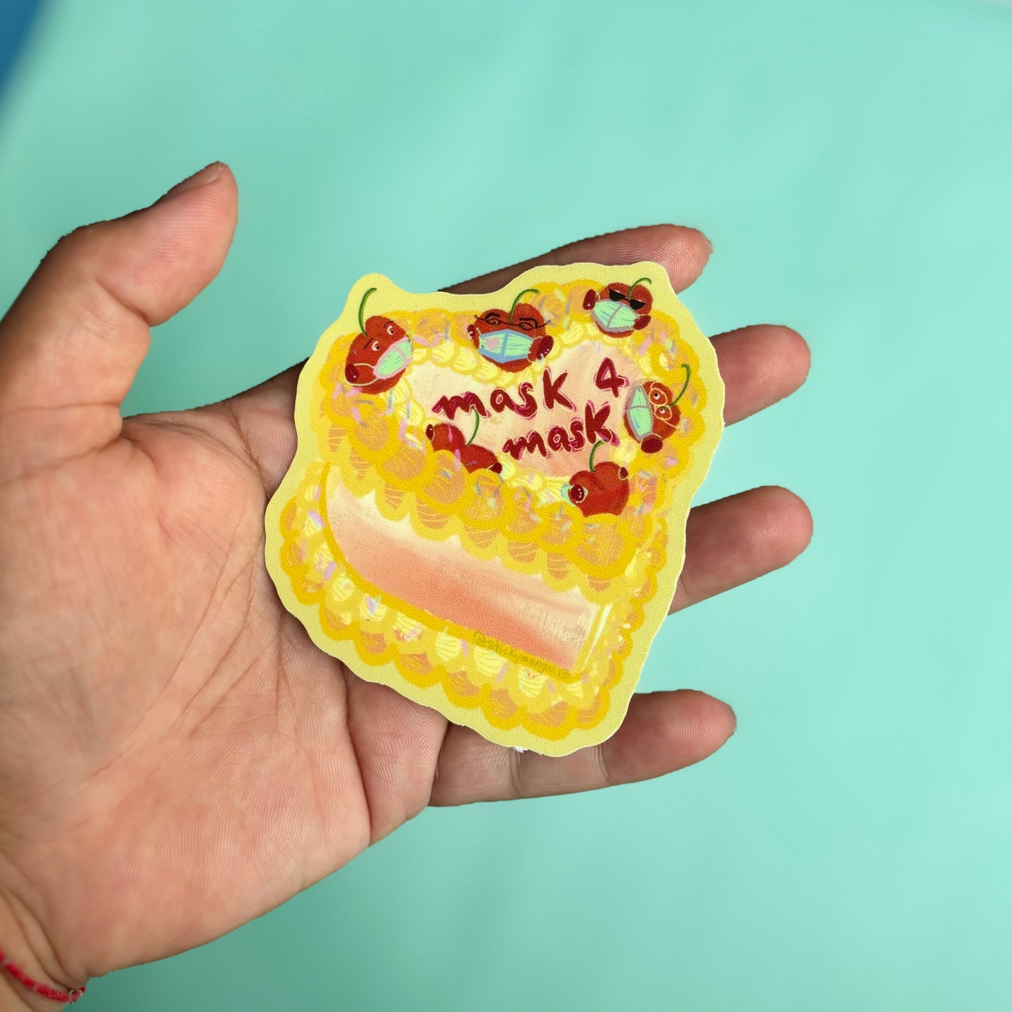 brown hand holding cake sticker. It's decorated with cherries wearing a mask, and reads 'mask 4 mask'