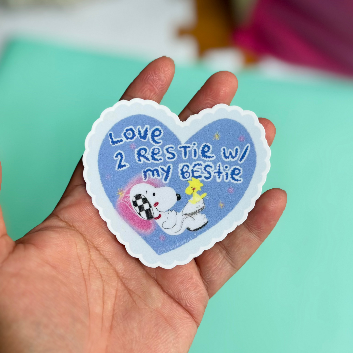 brown hand holding heartshaped sticker of a dog and bird